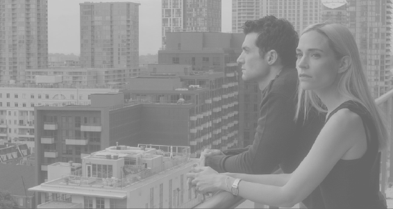 [Image Description: A man and a woman stand on a blacony. Both are leaning on the rail and looking out at the city of Toronto.]